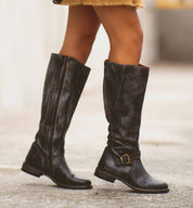 A woman wearing black Glaye riding boots and a yellow skirt. (Product Name: Glaye, Brand Name: Bed Stu)