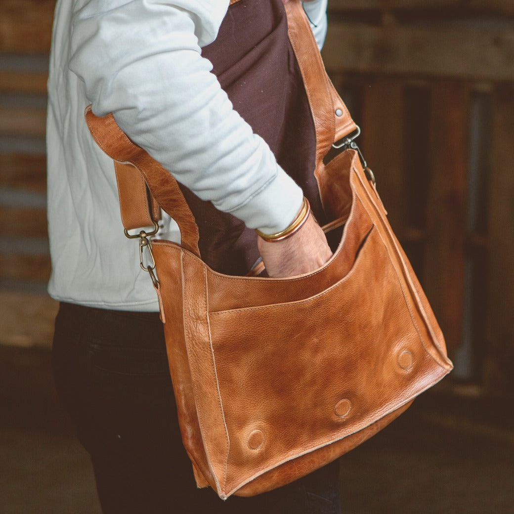 A man is holding a Bed Stu Hampton II tan leather bag.