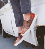 A person standing on the side of a truck wearing a pair of Harry slip on sneakers from Bed Stu.