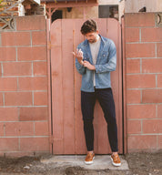A man leaning against a brick wall holding a Bed Stu cell phone named Harry.