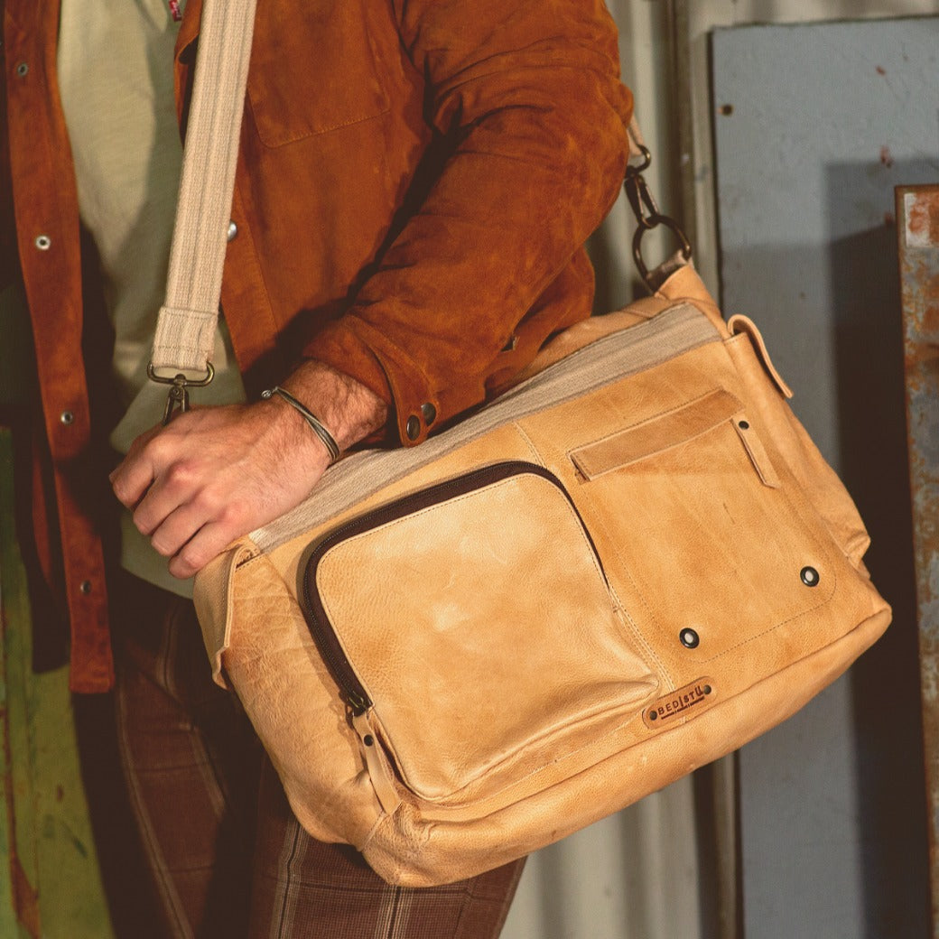 A man is holding a Bed Stu Hawkeye II tan leather messenger bag.