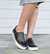 A woman wearing a pair of black Hermione slip on sneakers by Bed Stu.