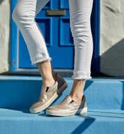 A woman wearing white jeans and tan Bed Stu slip on sneakers standing on a blue door.