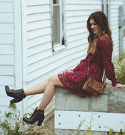 A woman in a Burgundy dress sitting on a wall wearing isla boots. (Brand Name: Bed Stu)