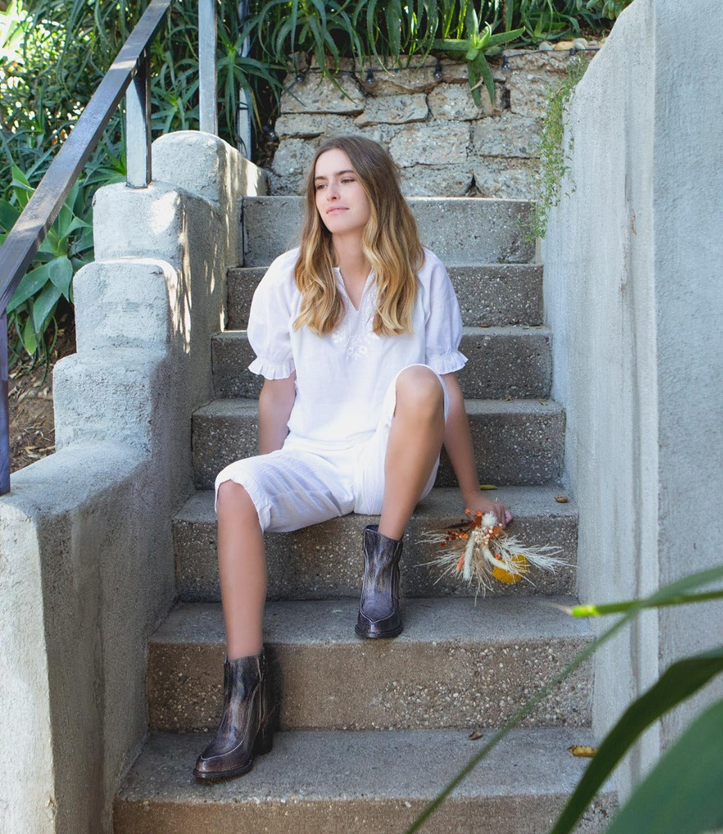 A young woman sitting on steps wearing Bed Stu Isla boots.
