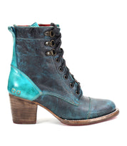 The Judgement boot by Bed Stu showcases a worn-look teal and dark blue leather design with an 8-eye lace-up, chunky wooden heel, metallic details, cushioned insole, and a cap-toe finish.