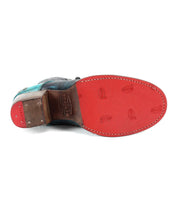 The image shows the sole of a Bed Stu Judgement boot, predominantly red with some wear marks and embossed with the branding. The heel is a comfortable block heel made of brown wood, showcasing its iconic design.