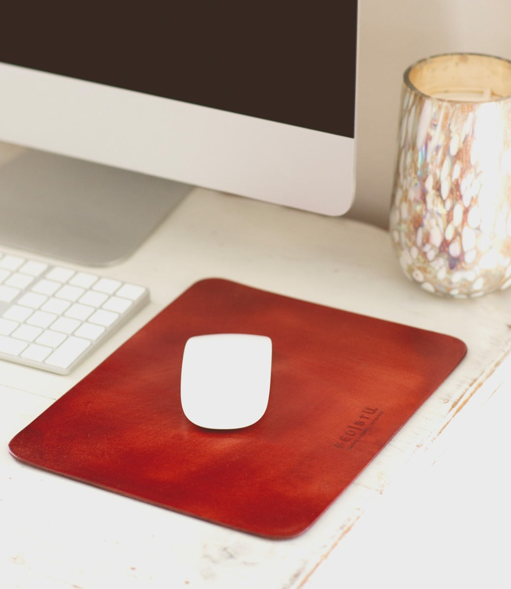 A red leather Launcher mouse pad on a desk next to a computer.