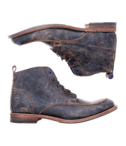 The Lincoln II boots by Bed Stu, crafted from brown leather with a distressed finish, are displayed side by side. One stands upright while the other, showcasing its 5-eye lace-up design, lies on its side to emphasize the intricate design and sole details. These versatile Lincoln II boots seamlessly transition from rugged workwear to a polished look.