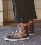 A person wearing a pair of brown Bed Stu Lordmind high top sneakers.