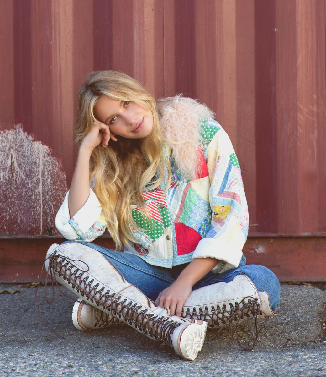 A woman sitting on the ground in a Lustrous jacket and Bed Stu boots.