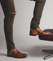 A man standing on a chair wearing Bed Stu Michelangelo brown leather shoes.