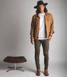 A man in a hat and jeans standing in front of a Bed Stu stool.