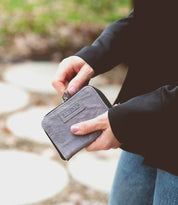 A woman holding a grey Bed Stu Ozzie wallet on a sidewalk.