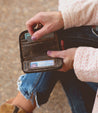 A woman is holding an Ozzie wallet while sitting on the ground.
