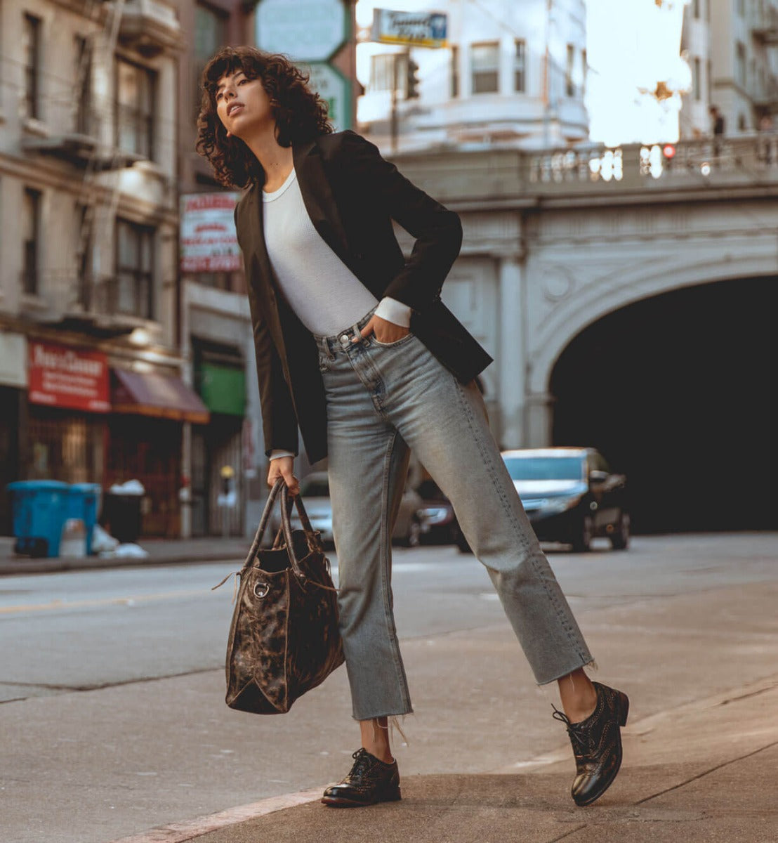 A woman in Bed Stu jeans and a Bed Stu blazer standing on a street.