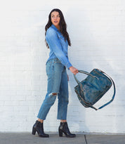 A woman in Rockaway jeans and Bed Stu boots holding a blue bag.