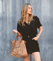 A woman in black shorts holding a Bed Stu Rockaway tote bag.