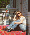A woman sitting on the steps of a house wearing Bed Stu sunglasses.