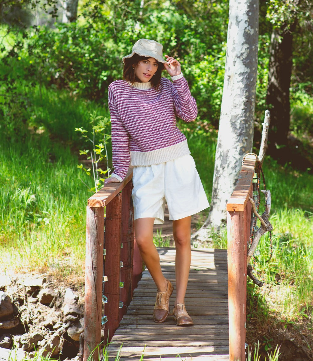 A woman standing on a bridge wearing a Bed Stu Rose sweater and shorts.