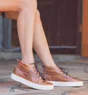 A woman wearing a brown Bed Stu Rossela crocodile high top sneaker.