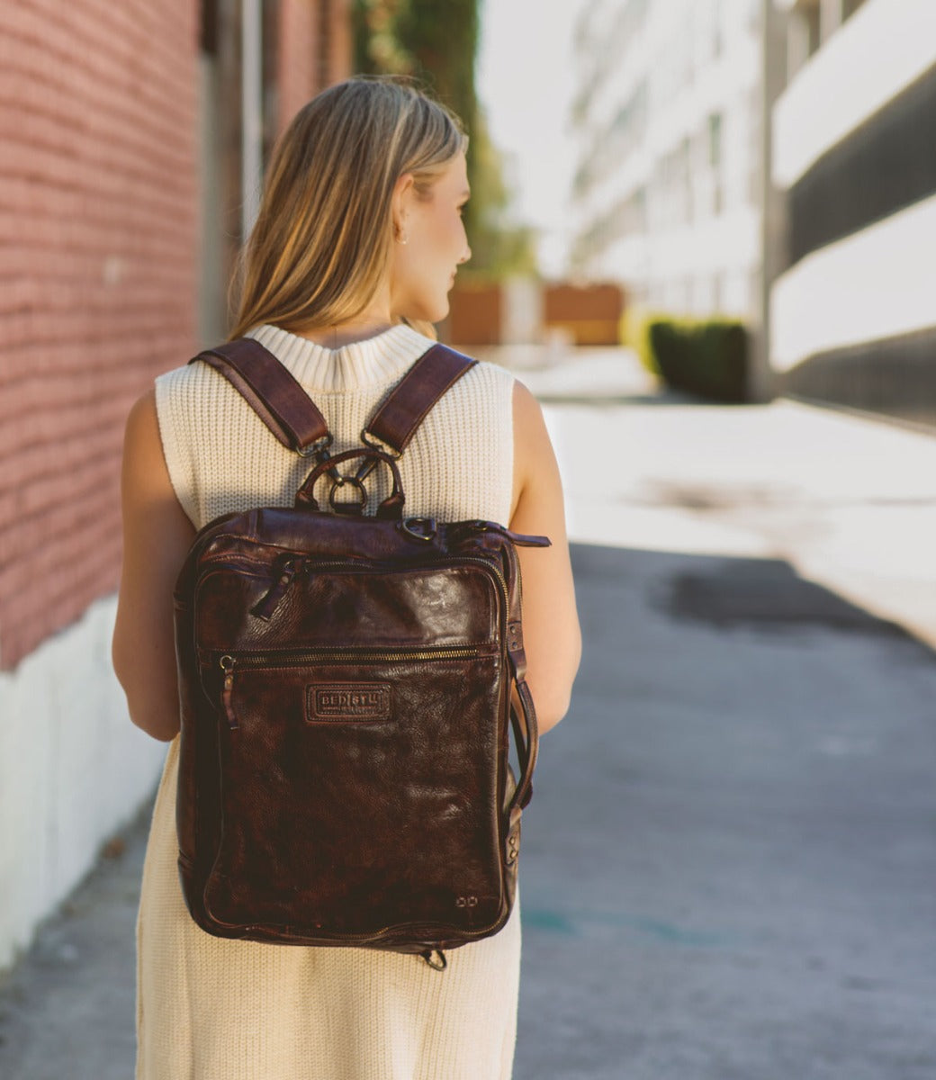 A woman wearing a brown leather Socrates backpack made by Bed Stu walking down the street.