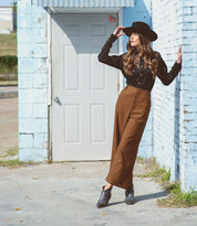 A woman leaning against a wall wearing a Tania hat and wide leg pants by Bed Stu.