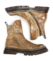 The Bed Stu Tanto boots are a pair of worn brown leather men's boots with side zippers, metal studs along the seam, and a rugged lug outsole, shown side by side on a white background for European flair.