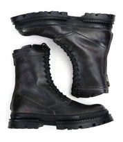 The Bed Stu Tempt is a pair of black leather combat boots with thick, rugged soles, stylishly shown from side and sole views against a white background.