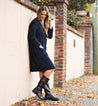 A woman is leaning against a wall in a Bed Stu Gogo Lug Wide Calf coat and boots.