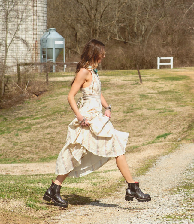 A woman in a Valda Hi dress by Bed Stu walking down a dirt road.