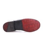 The underside of the Bed Stu Yurisa black shoe has a Vibram outsole with a two-toned design: red front and heel sections featuring raised text, while the middle section is black and displays signs of wear.