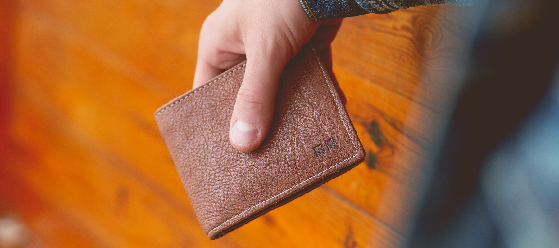 Close up of man holding a brown wallet in front of stained wood.