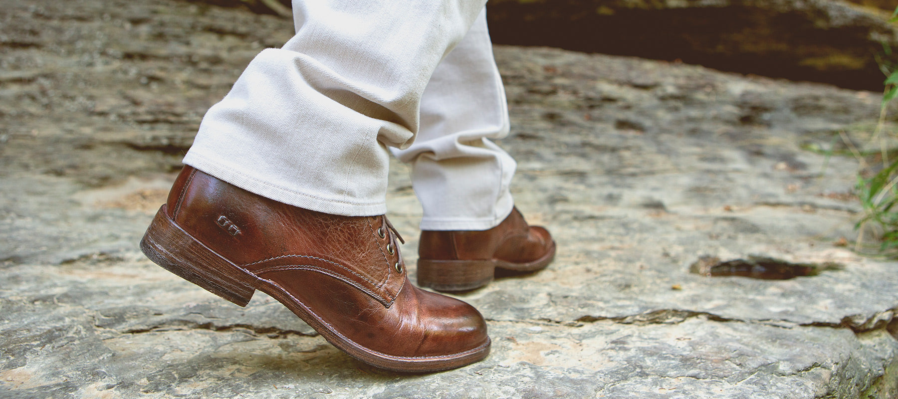 Close up of man walking in brown dress shoes with cream colored pants on rock ledge.
