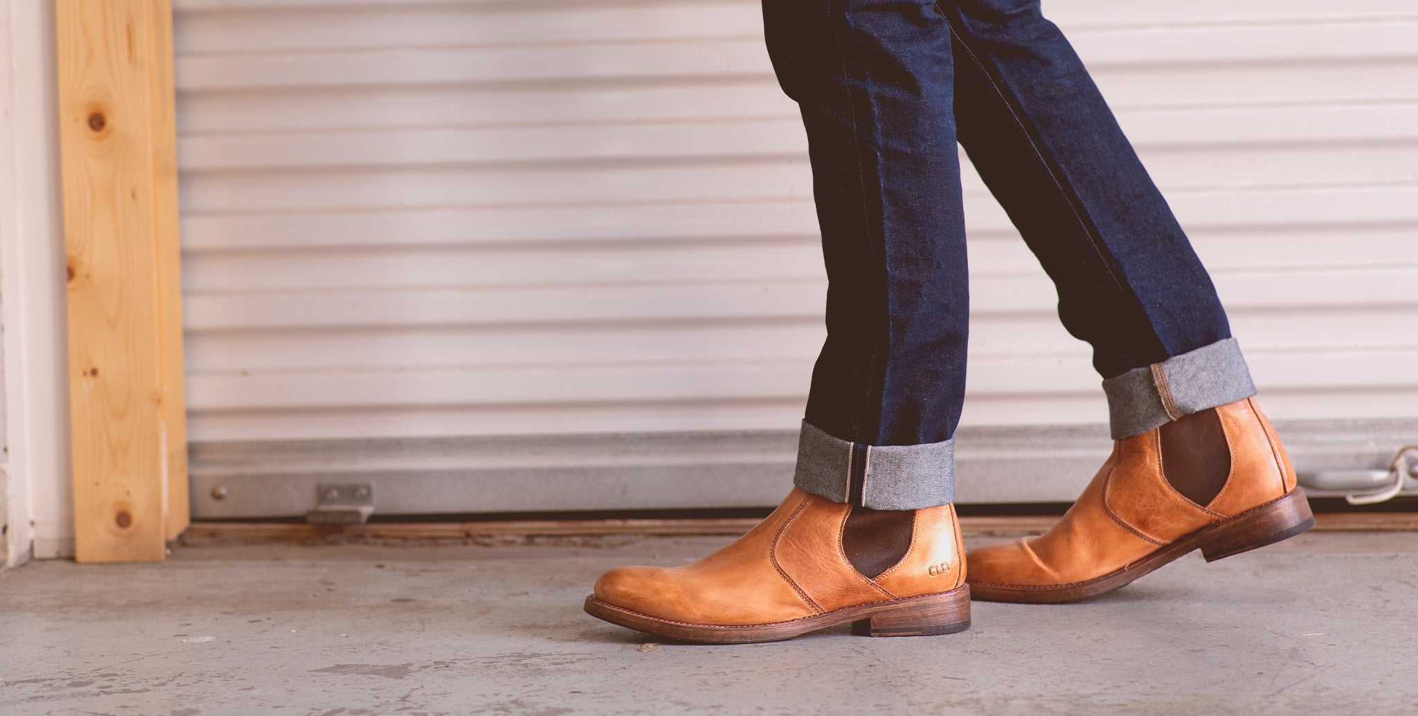 Man wearing tan boots with blue jeans walking in front of garage door.