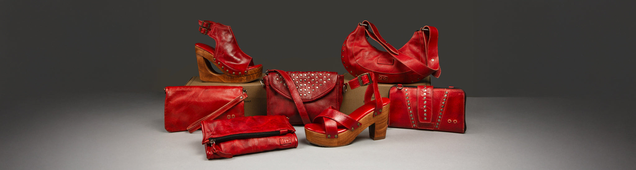 Various red leather bags and shoes with studs arranged on a textured surface; a person holds a similar handbag on the right.