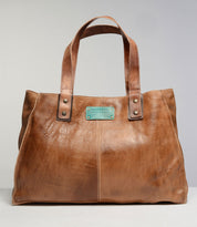 The Studio Arlington Body, a brown leather tote bag by Bed Stu, features two handles and a stitched rectangular patch with the text "BEDSTU." Rivet details at the handle bases add an extra touch of style. Displayed against a plain background, this personalized bag is perfect for showcasing your own style and creativity.
