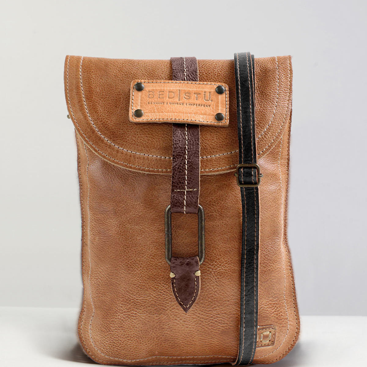 A Studio Sterling Body crossbody bag from Bed Stu is displayed against a neutral background. This brown leather bag features a front buckle and an adjustable black strap, with the brand label "Bed Stu" prominently visible on the flap, adding a touch of creativity to your own style.
