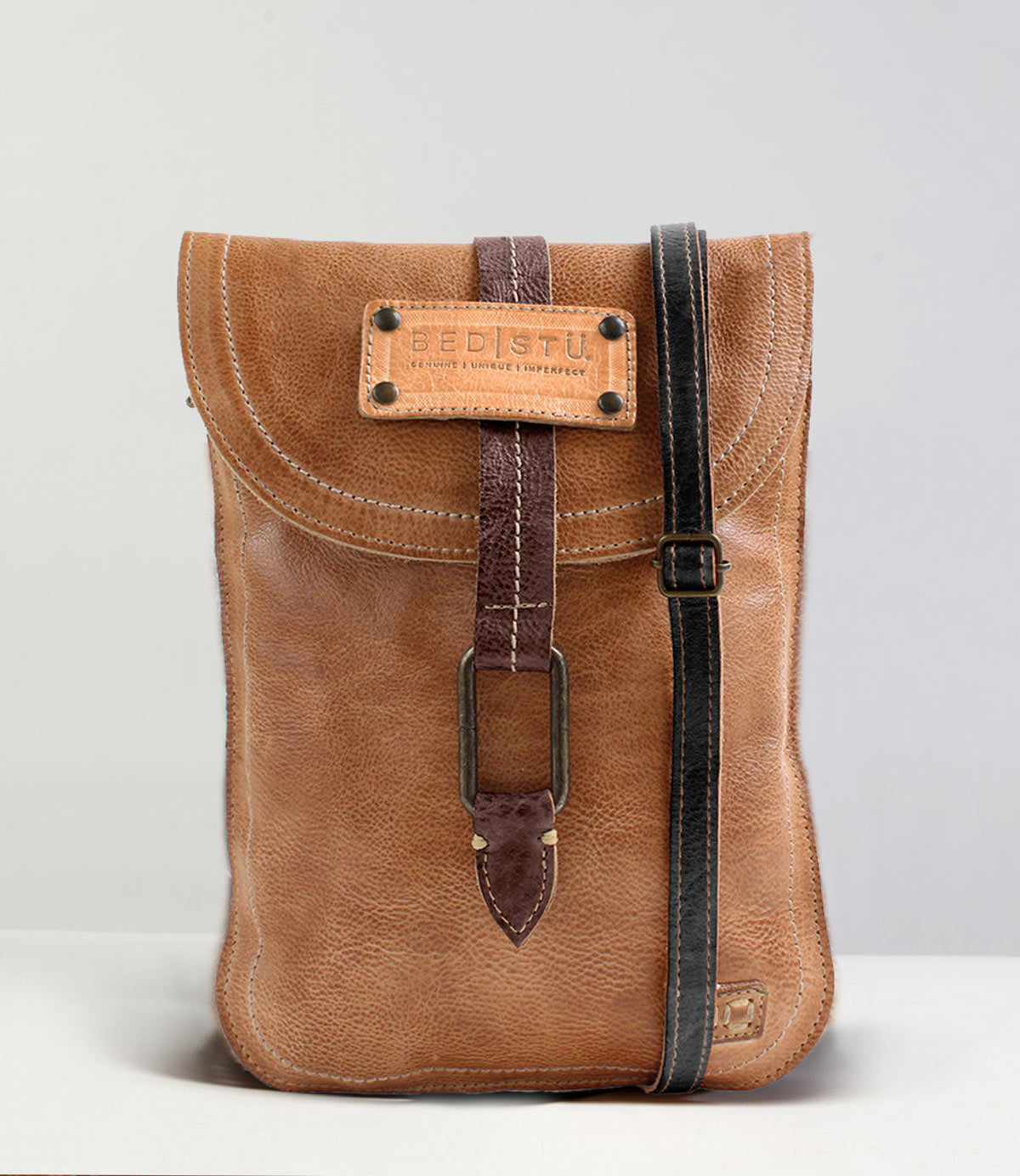 A Studio Sterling Body crossbody bag from Bed Stu is displayed against a neutral background. This brown leather bag features a front buckle and an adjustable black strap, with the brand label "Bed Stu" prominently visible on the flap, adding a touch of creativity to your own style.