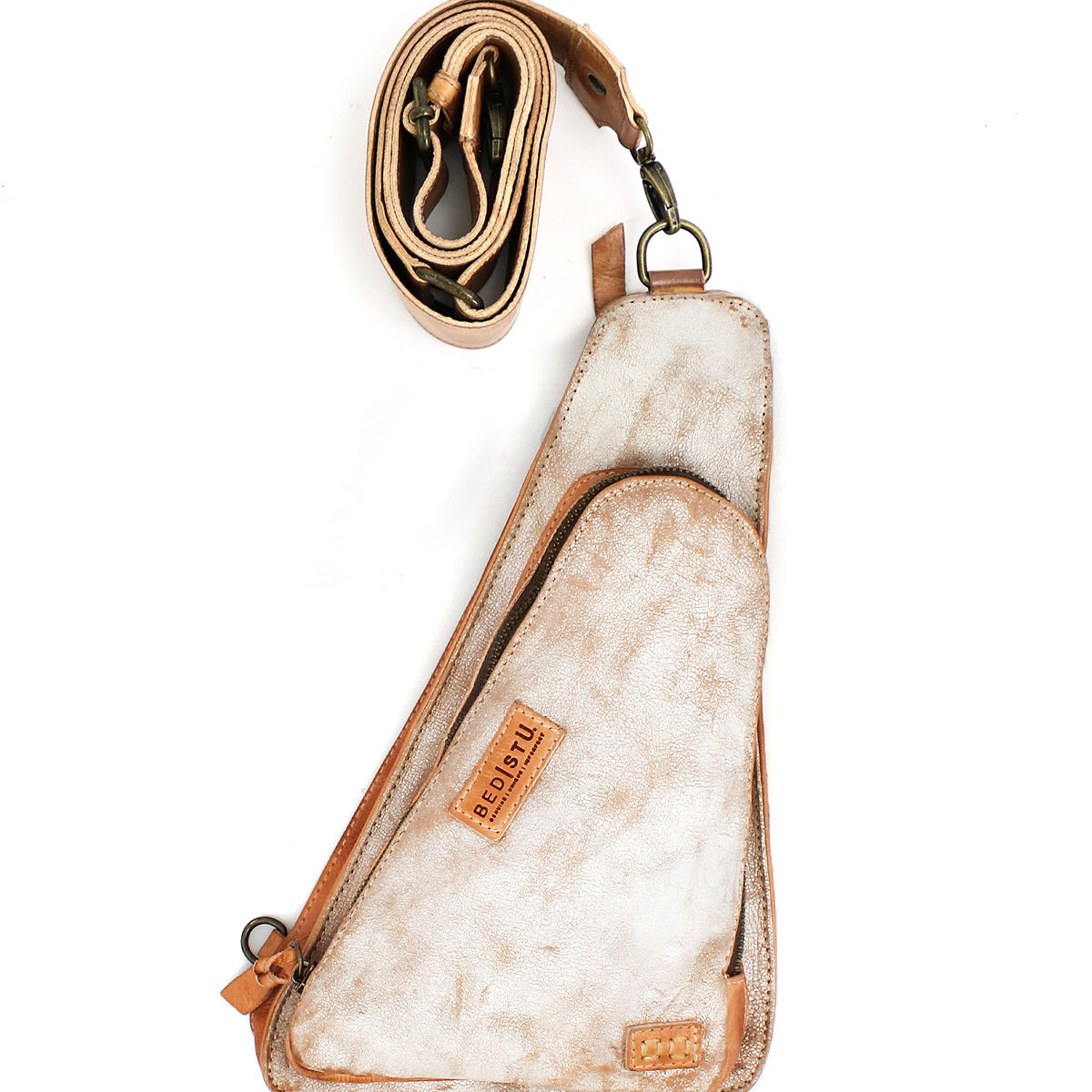The Bed Stu Adept is a triangular crossbody sling bag crafted from vegetable-tanned leather, featuring a visible brand label and a detached coiled strap, shown against a white background.