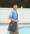 A woman in a hat and leopard skirt standing next to a pool, confidently carrying the Bed Stu Aiken, a convertible crossbody bag made of vegetable-tanned leather.