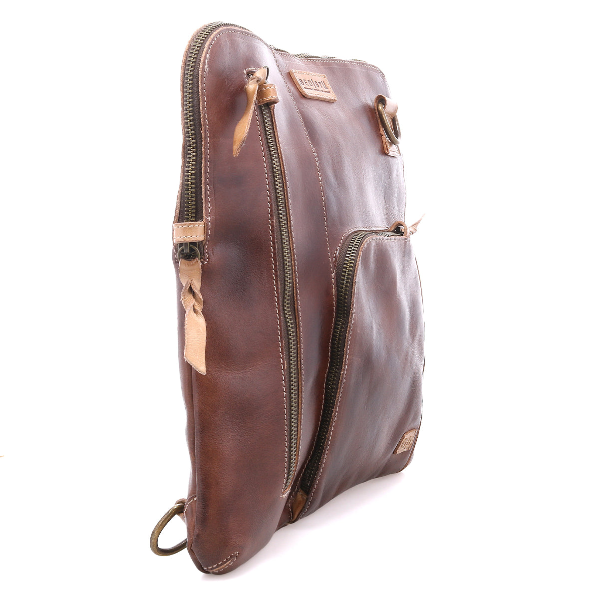 The Bed|Stü Aiken is a brown full-grain leather zippered pouch shown standing upright at an angle, featuring two zippered compartments, anti-theft security features, and a brand tag on the front.