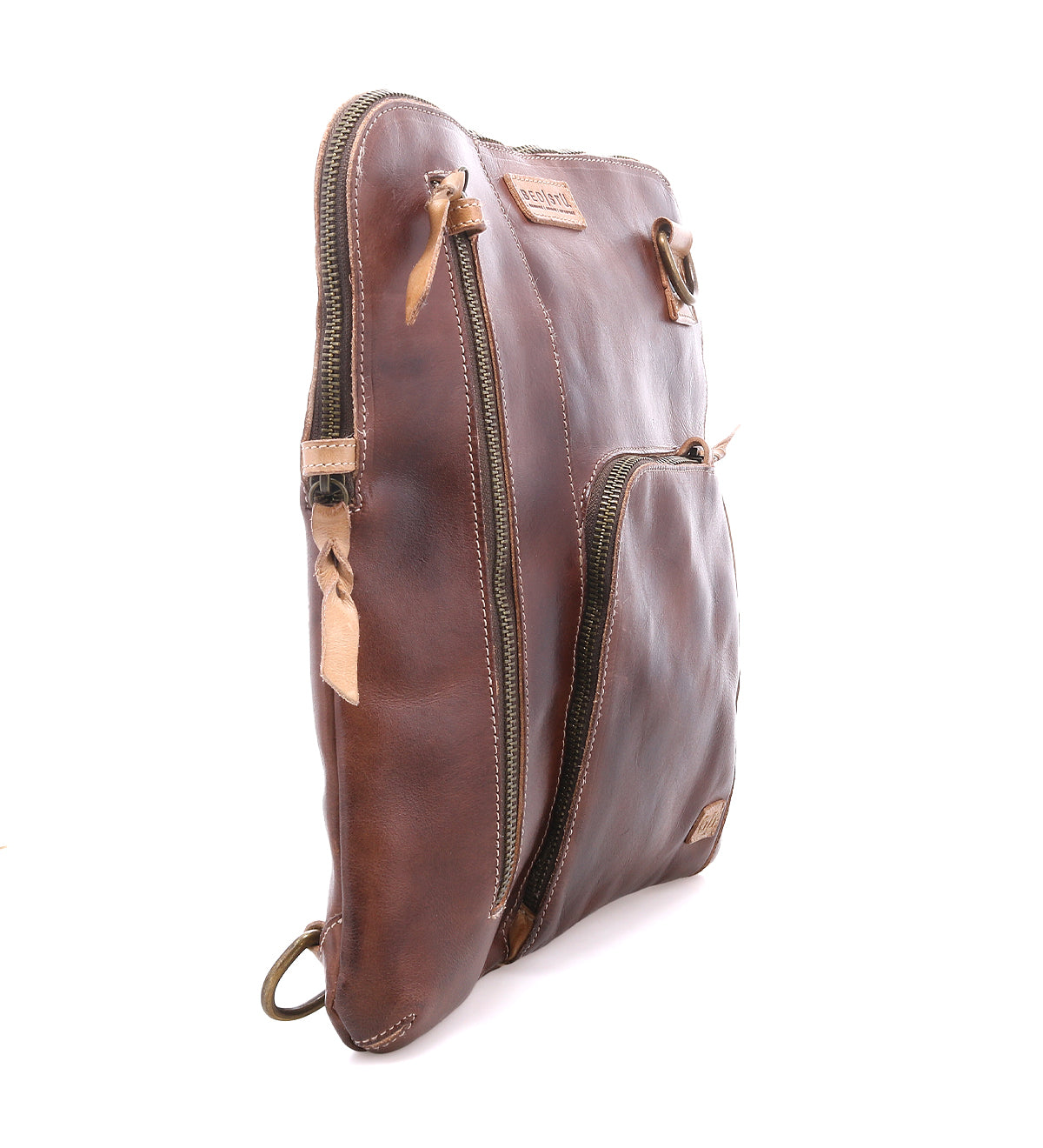 The Bed|Stü Aiken is a brown full-grain leather zippered pouch shown standing upright at an angle, featuring two zippered compartments, anti-theft security features, and a brand tag on the front.