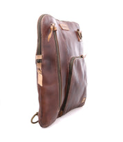 The Bed Stu Aiken is a brown full-grain leather pouch featuring two zippered compartments, tan pull tabs, and a ring attachment on the bottom corner, shown against a white background.