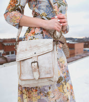 A woman in a floral dress holding a Bed Stu Ainhoa crossbody handbag.