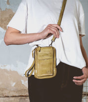 A person in a white t-shirt and jeans is holding Bed Stu's Alelike, a small yellow crossbody phone holder, ideal for everyday functionality.