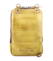 The Alelike by Bed Stu is a stylish yellow leather bag with a zippered top and brown metal rings, crafted from premium leather. It elegantly functions as a chic crossbody phone holder, with the brand name embossed at the bottom.