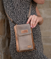 A person in a patterned dress holds the compact brown Alelike crossbody bag by Bed Stu against a stone wall.