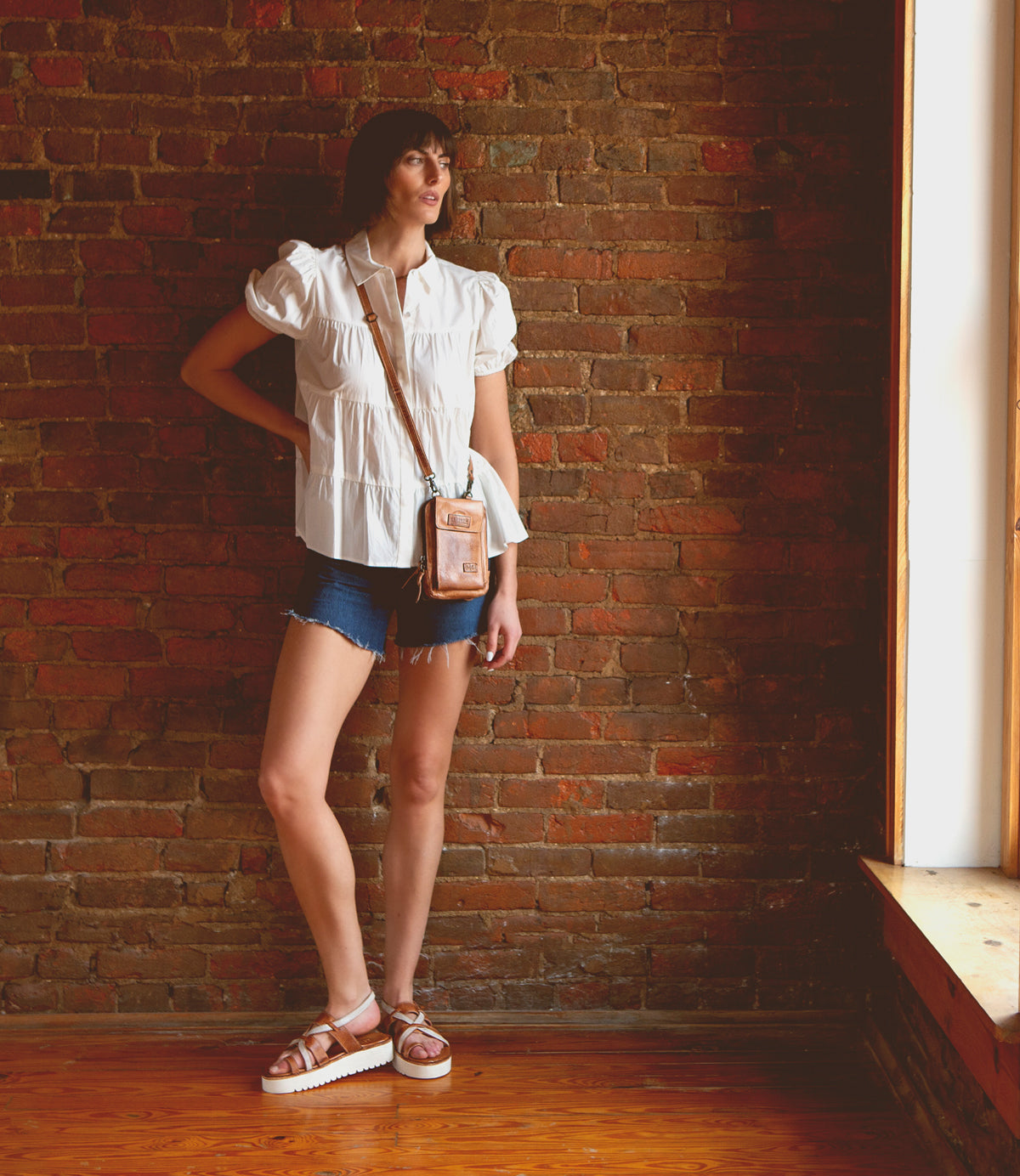A woman standing in front of a brick wall wearing shorts and a Bed Stu Alelike premium leather purse.