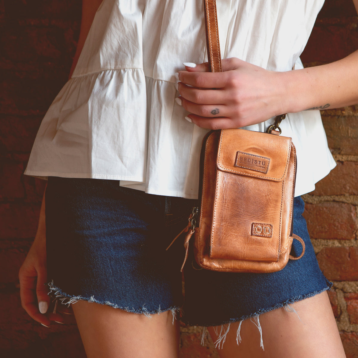 A woman in denim shorts holding a Bed Stu Alelike premium leather crossbody bag.